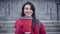 Unrecognizable blurred Caucasian woman stretching coffee cup to camera and smiling. Young lady in red coat and gloves