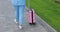 Unrecognizable businesswoman rolls a suitcase goes along sidewalk