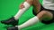 Unrecognizable Caucasian football player with ache in leg sitting on green screen. Young footballer with painful limb at