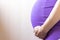 Unrecognizable Close up Pregnant women. Hands over tummy during last month of pregnancy. In violet color dress on light