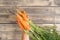 Unrecognizable cropped man hand hold orange tasty juicy carrot with green stem and leaves on wooden background. Top view