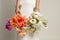 Unrecognizable cropped woman in white elegant silk dress with two bouquets of colorful flowers in hands with accessories
