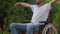 Unrecognizable disabled man in wheelchair stretching hands sitting outdoors on spring summer day. Optimistic African