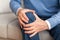 Unrecognizable elderly man massaging knee sitting on couch at home