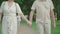 Unrecognizable elegant mid-adult man and woman holding hands and strolling in summer park. Loving Caucasian couple