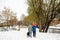 Unrecognizable family in winter casual outfit walking with kid and dog in snowy park near river