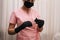 Unrecognizable female nurse in pink coat holds syringe with needle in her gloved hands for vaccination or injecting patient.