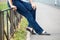 Unrecognizable female sitting on steel fence of pedestrian pathway, blue jeans and comfortable shoes