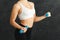 Unrecognizable fitness woman with dumbbells standing at grey background