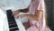 An unrecognizable girl plays the digital piano in a soft pink velvety dress.