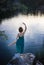 Unrecognizable girl stands with her back on a stone in front of smooth surface of water in a graceful dance pose