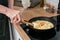 Unrecognizable hands of man taking out fresh omelette from frying pan with wooden paddle on black electric cooker