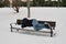 Unrecognizable homeless man sleeping on bench in snowy cold winter