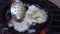 Unrecognizable latin farmer person cooking fried hake fish in a frying pan, on a metal grill with red hot firewood