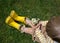 Unrecognizable little boy in bright yellow rubber boots with a bouquet of daisies sits on the grass