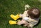 Unrecognizable little boy in yellow rubber boots with a bouquet of daisies sits on green grass