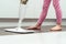 Unrecognizable little preteen girl wearing blue T-shirt, pink leggings, holding white handheld spray mop, mopping floor.