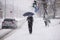 An unrecognizable man with a face mask and umbrella stands in city during a snowstorm