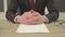 Unrecognizable man in the suit sitting at the table with crossed fingers in front of blank papers, pens and glasses. Big