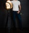 An unrecognizable man in a white T-shirt stands near a spotlight in a dark room