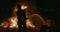 Unrecognizable men silhouette on bonfire background extinguishes fire with hose