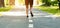 Unrecognizable millennial guy running along asphalt road at urban park, closeup of legs