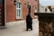 Unrecognizable mysterious man in dark black raincoat walking along red brick wall in old european town