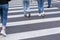 Unrecognizable people in casual clothes cross the road at a pedestrian crossing. Crosswalk road surface marking.