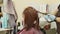 Unrecognizable person dyes hair of young woman in salon. Unknown hairdresser in gloves coloring hair of client in beauty