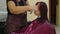 Unrecognizable person shears hair of young woman in salon. Unknown hairdresser cuts bangs of client in beauty salon