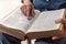 unrecognizable person sitting studying the bible with selective focus on his finger pointing to a bible passage