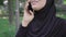 Unrecognizable positive muslim woman talking on the phone in sunny summer park. Close-up portrait of excited Middle