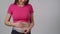 Unrecognizable pregnant woman measuring her belly with a measuring tape while standing on a white background. A pregnant