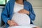 Unrecognizable pregnant woman sitting indoors at home.