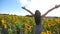 Unrecognizable pretty girl standing among big field with blooming sunflowers and raising hands. Woman having relax or