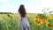 Unrecognizable pretty girl walking among blooming sunflowers. Young woman in dress going through field enjoying freedom