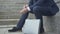 Unrecognizable secret agent sitting on urban stairs with attache case chained to his hand with handcuffs. Caucasian man