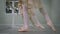 Unrecognizable slim ballerinas rehearsing tendu and plie ballet movements at barre in dance studio. Female legs moving