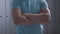 Unrecognizable strong sportsman in blue T-shirt crossing hands as standing in locker room. Athletic Caucasian man posing