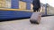 Unrecognizable successful businessman in black formal suit walking along platform and pulling suitcase on wheels. Young