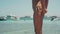 Unrecognizable tanned slim Caucasian woman in bikini standing on beach of lagoon with yachts at background. Adult female