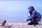 Unrecognizable teen boy feeding pigeons in winter rocky beach on sea backround.