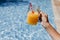 Unrecognizable teenager girl at the pool holding a jug of healthy orange juice and having fun outdoors. Summertime and lifestyle