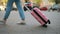 Unrecognizable tourist woman rolls a suitcase goes along sidewalk in city