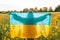 Unrecognizable ukrainian patriot woman standing with national flag in canola yellow field. Rare, back view. Ukraine