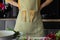 Unrecognizable woman with arms akimbo in striped kitchen apron with wooden spatula utensil. Chef cook fresh food at home