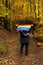 Unrecognizable woman in a beech forest standing raising over her head a rainbow flag in autumn in the rain