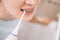 Unrecognizable woman with braces on her teeth brushing her teeth with by using a irrigate, close-up, before mirror.