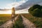 Unrecognizable woman dressed in shorts, jacket and cowboy boots walking through sunset field. copy space