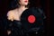 Unrecognizable woman dressed in style of art deco holding vinyl record on dark background. Roaring twenties, Flappers